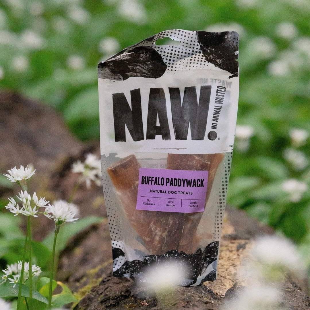 Package of NAW Buffalo Paddywack dog treats on a natural background with flowers.