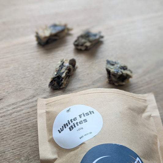 A close up of the brown bag focusing on the round white label with the name "white fish bites". The white fish skin treats can be seen in the background spilling out of the bag