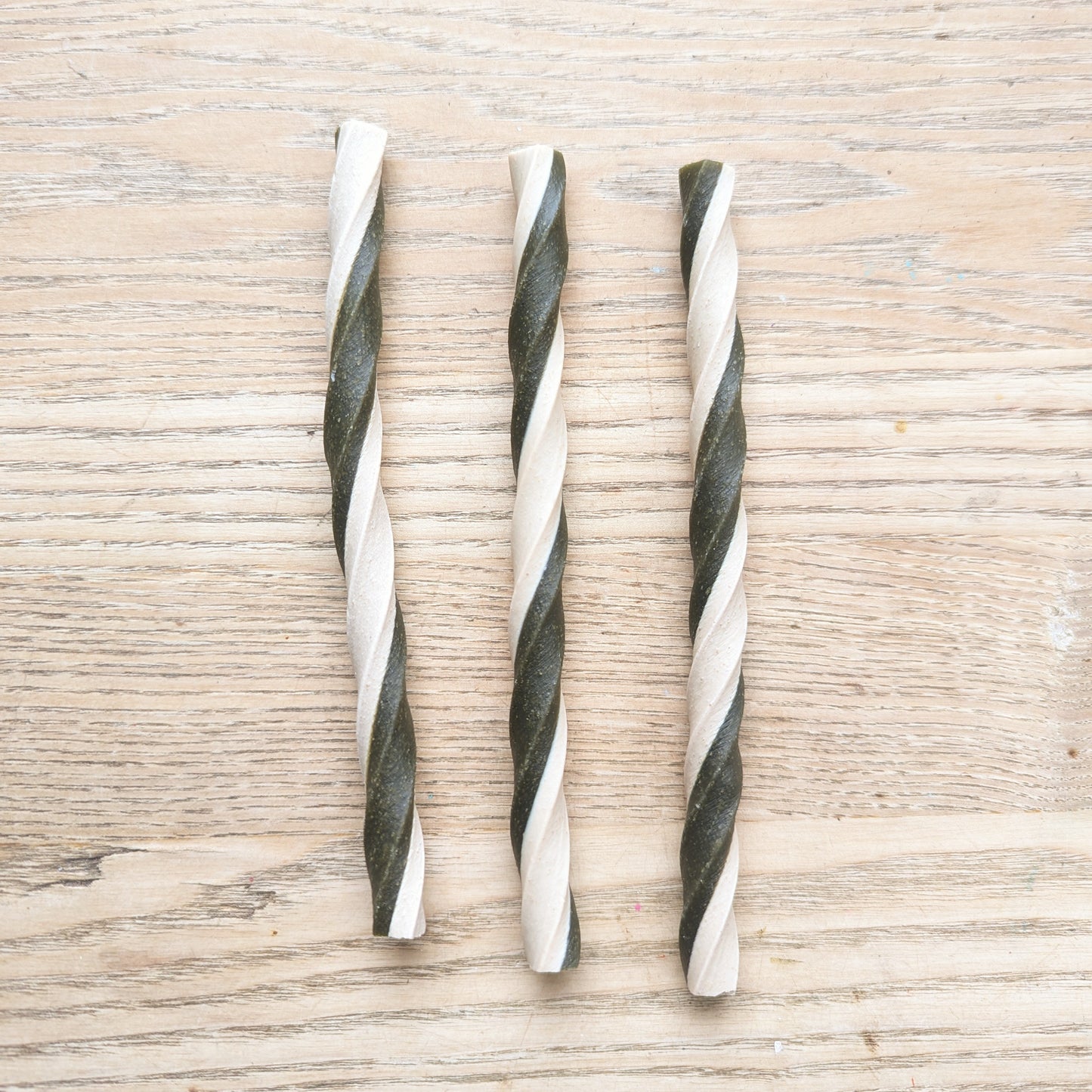three apple and spinach veg chew twists lying vertically next to each other. The are twisted white and green