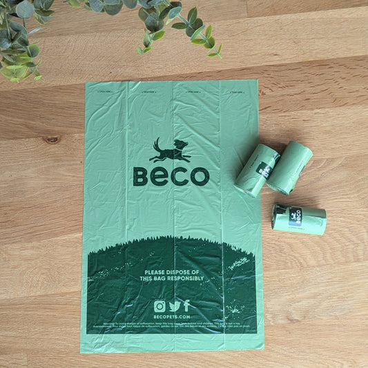 a single green beco bag opened fully, flat on a table. There is three rolls of bags on the right of the bag.