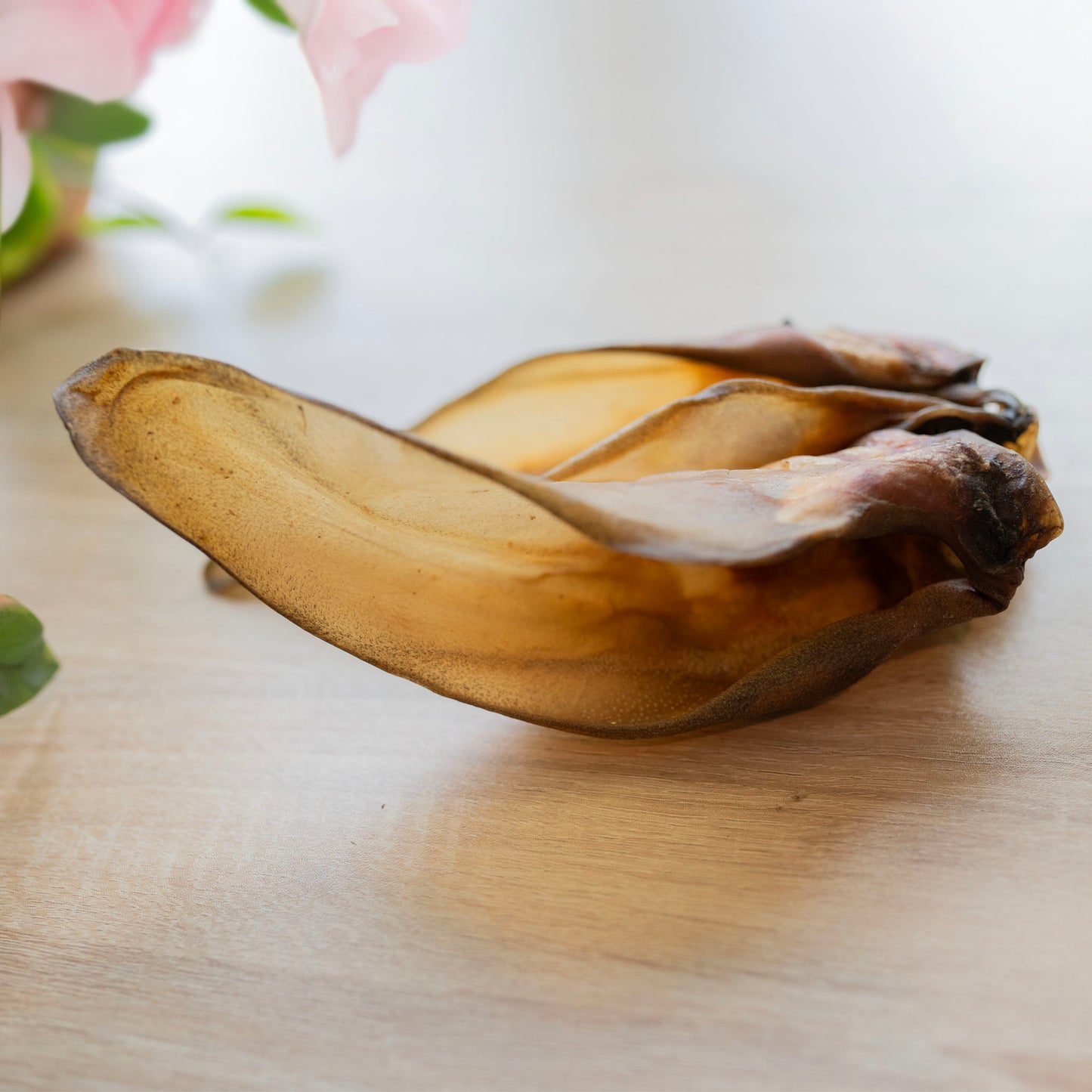two buffalo ears on a table, camera angle is looking at them from the side, so it looks like there's only one ear. The light is bright behind and there is a pink flower blurred at the back. The photo looks elegant