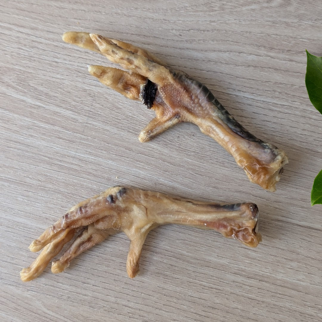 Two dried chicken feet snacks placed on a light wood grain surface.