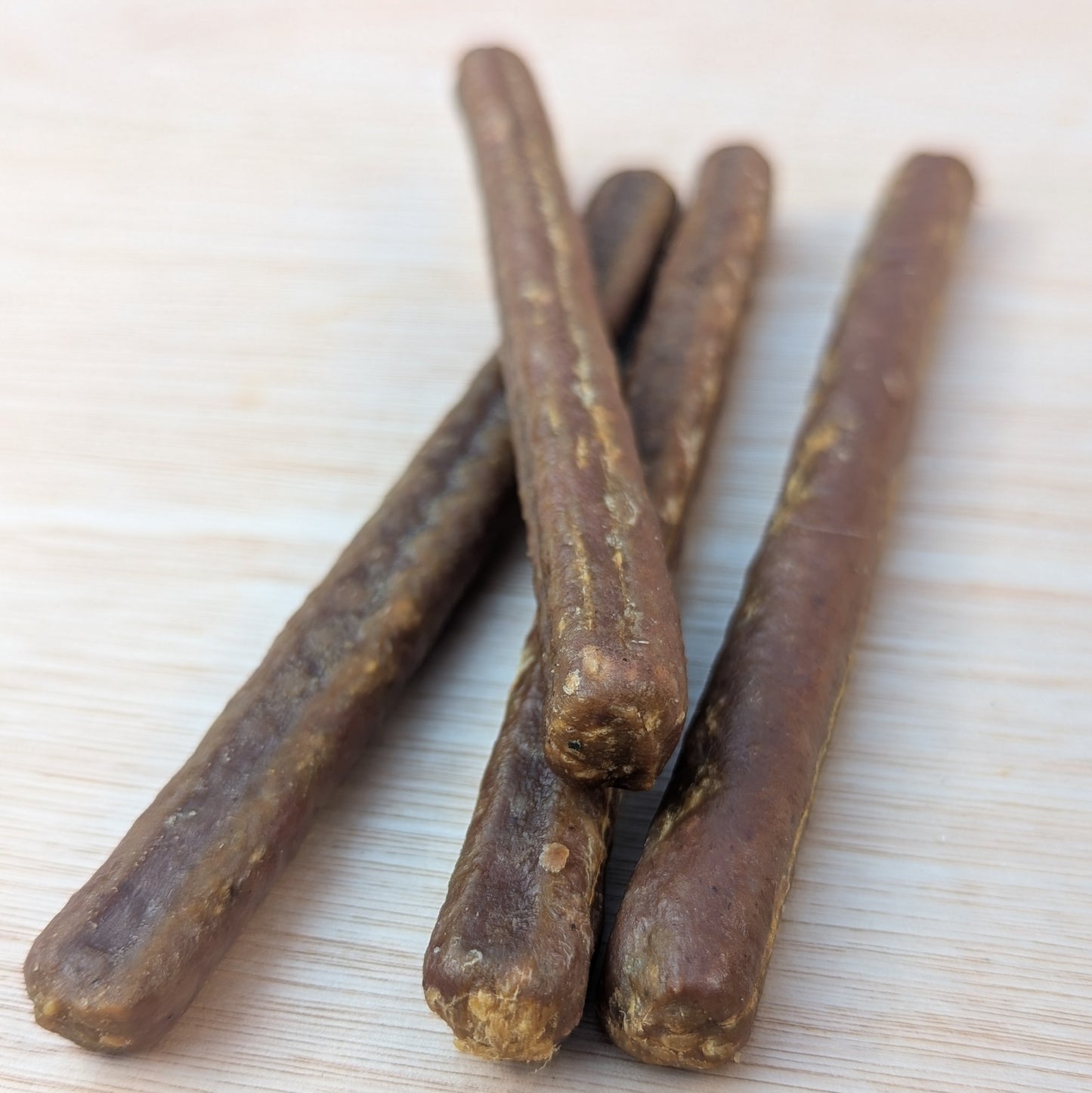 a close up of four long brown pure duck meat sticks, one is lying on top of the others