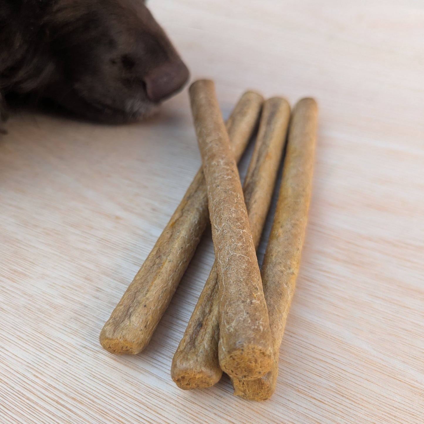 a close up of four pure salmon sticks, one is lying on top of the others. A brown spaniel nose is sniffing them in the top left corner