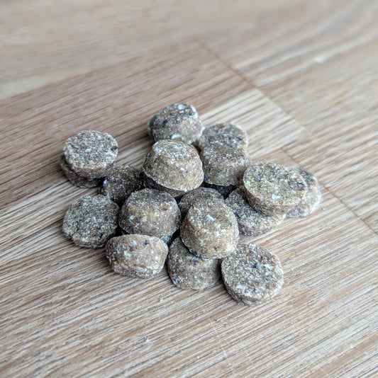 a close up of the training bites. There is a handful on a wooden table. They are small and circular, the top of the treat is less wide than the bottom