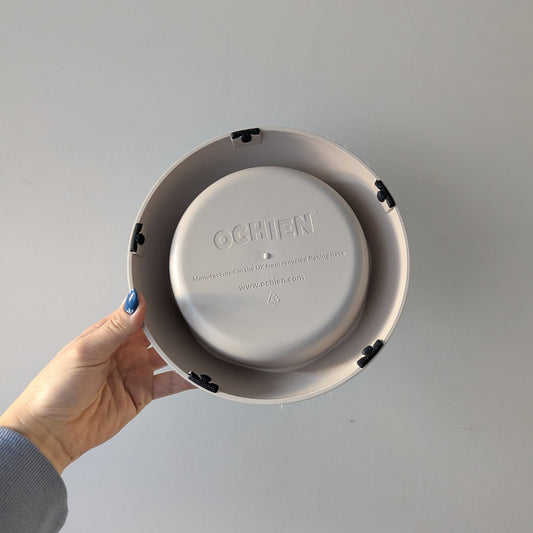 A cream coloured (colour stone) dog bowl is being held against a plain wall, showing the five non-slip pads on the bottom of the bowl