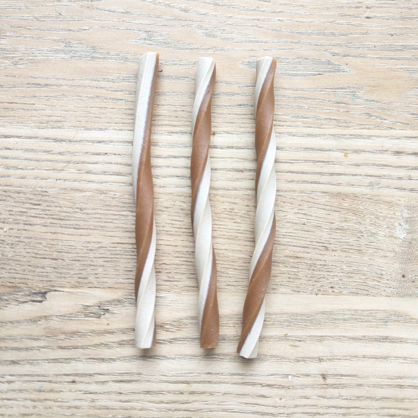 three peanut butter veg chew twists lying vertically next to each other. The are twisted white and brown