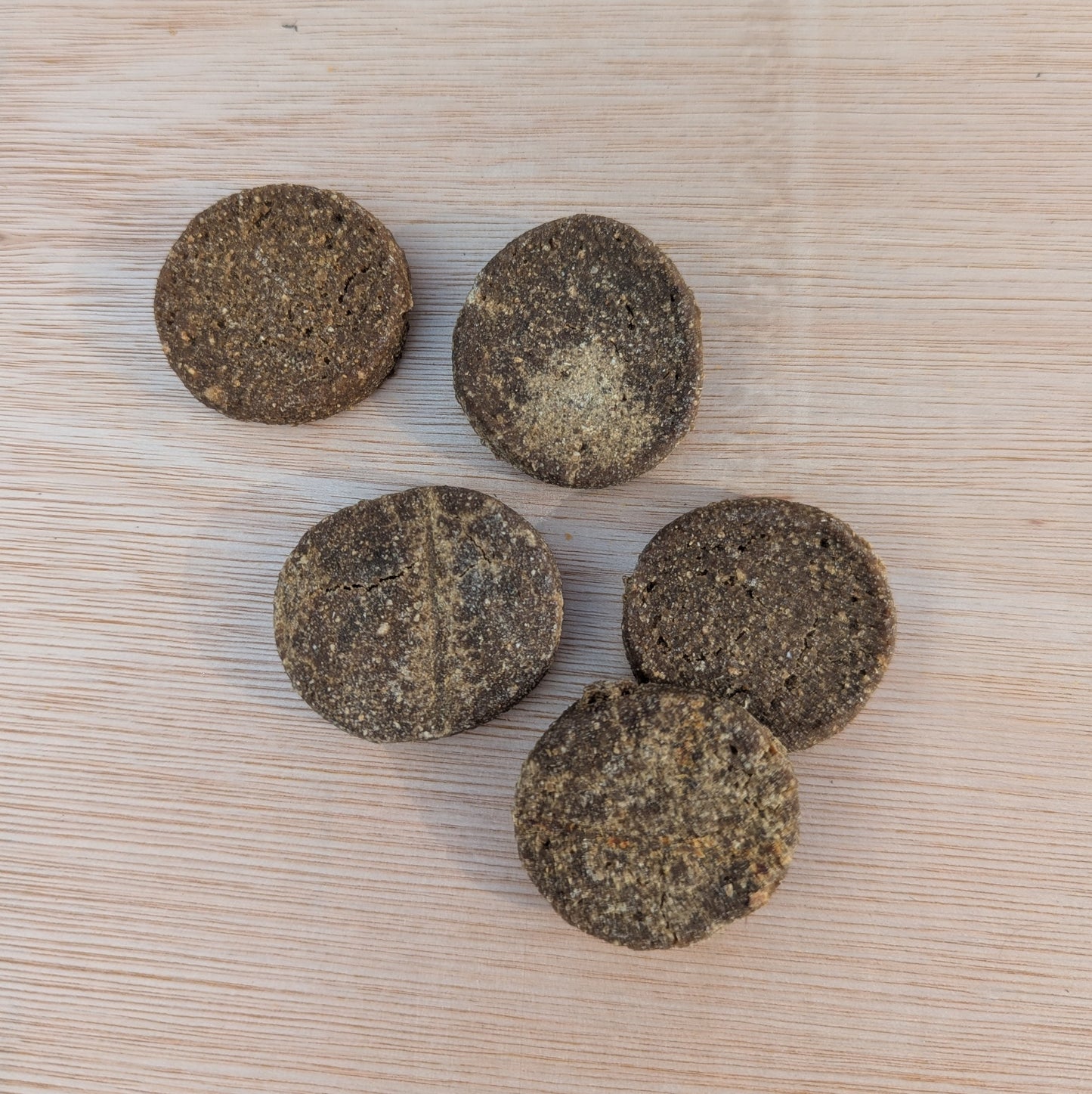 five round salmon cookies on a wooden ply board, approximately the size of a two-pound coin
