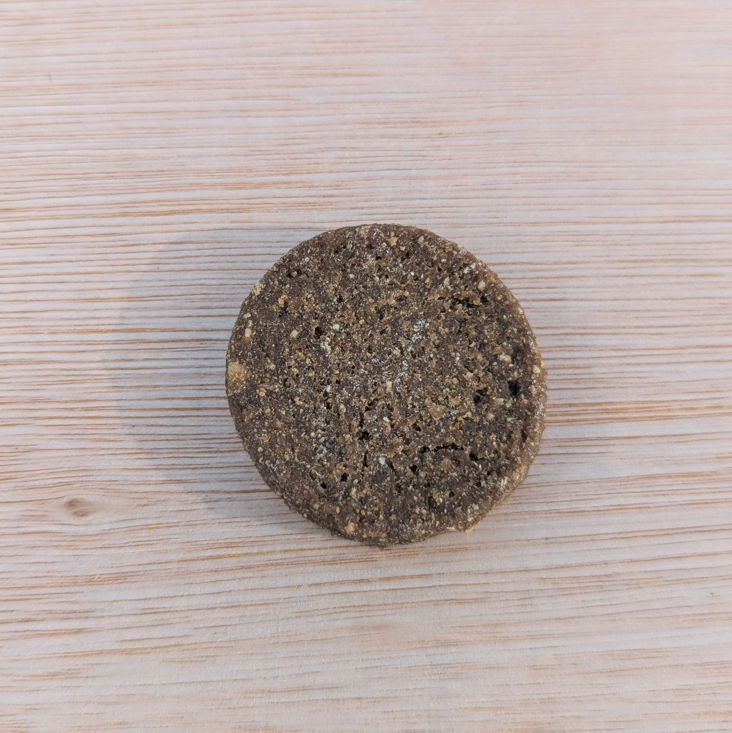 close up of a single round salmon cookie on a wooden table. It's dark brown with flecks of light brown