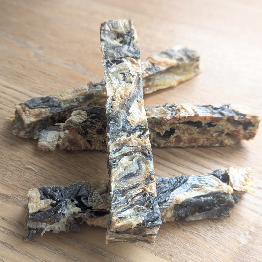 four white fish finger dog chews, one is lying on top of the others