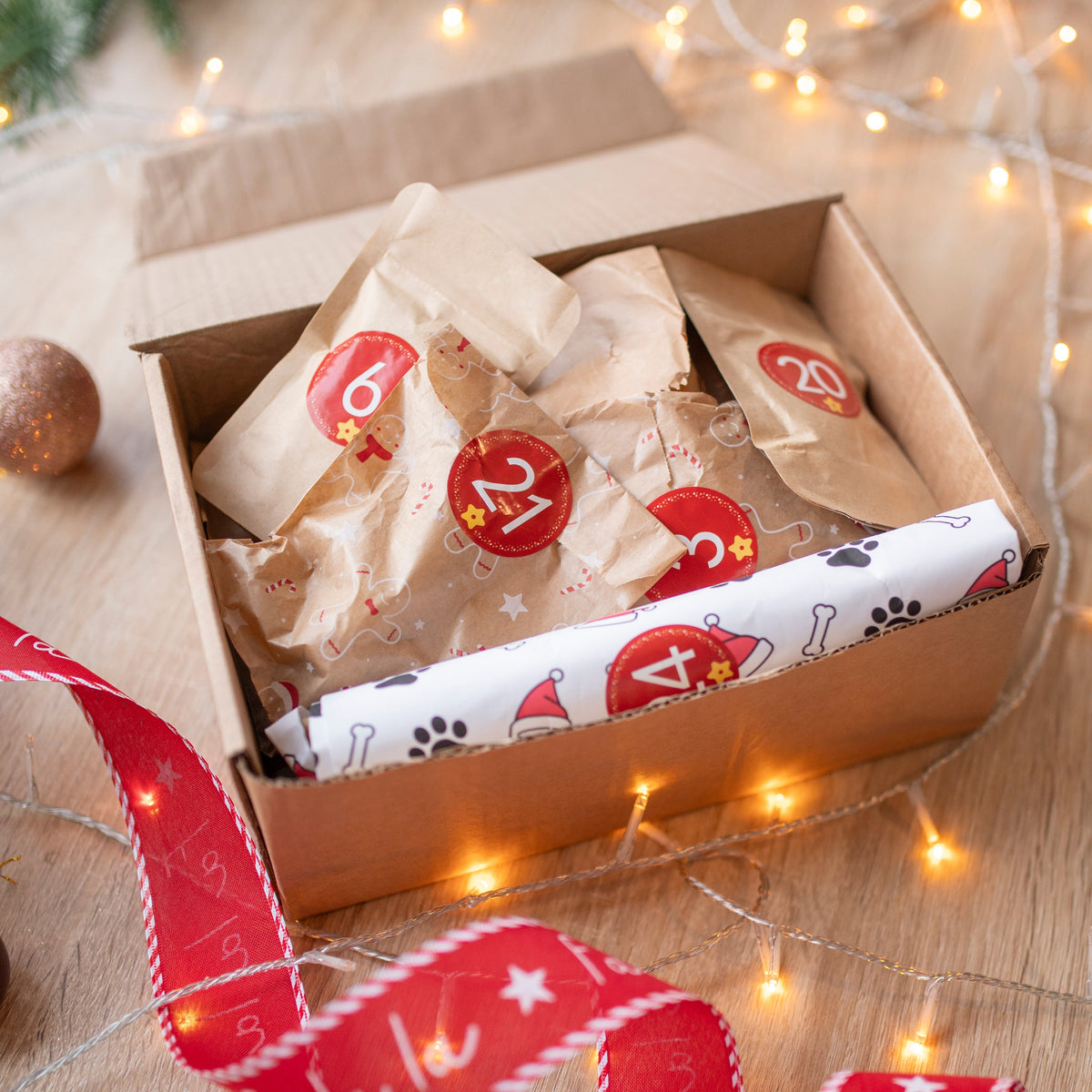A dog advent calendar with wrapped items and festive ribbons on a wooden surface with string lights.