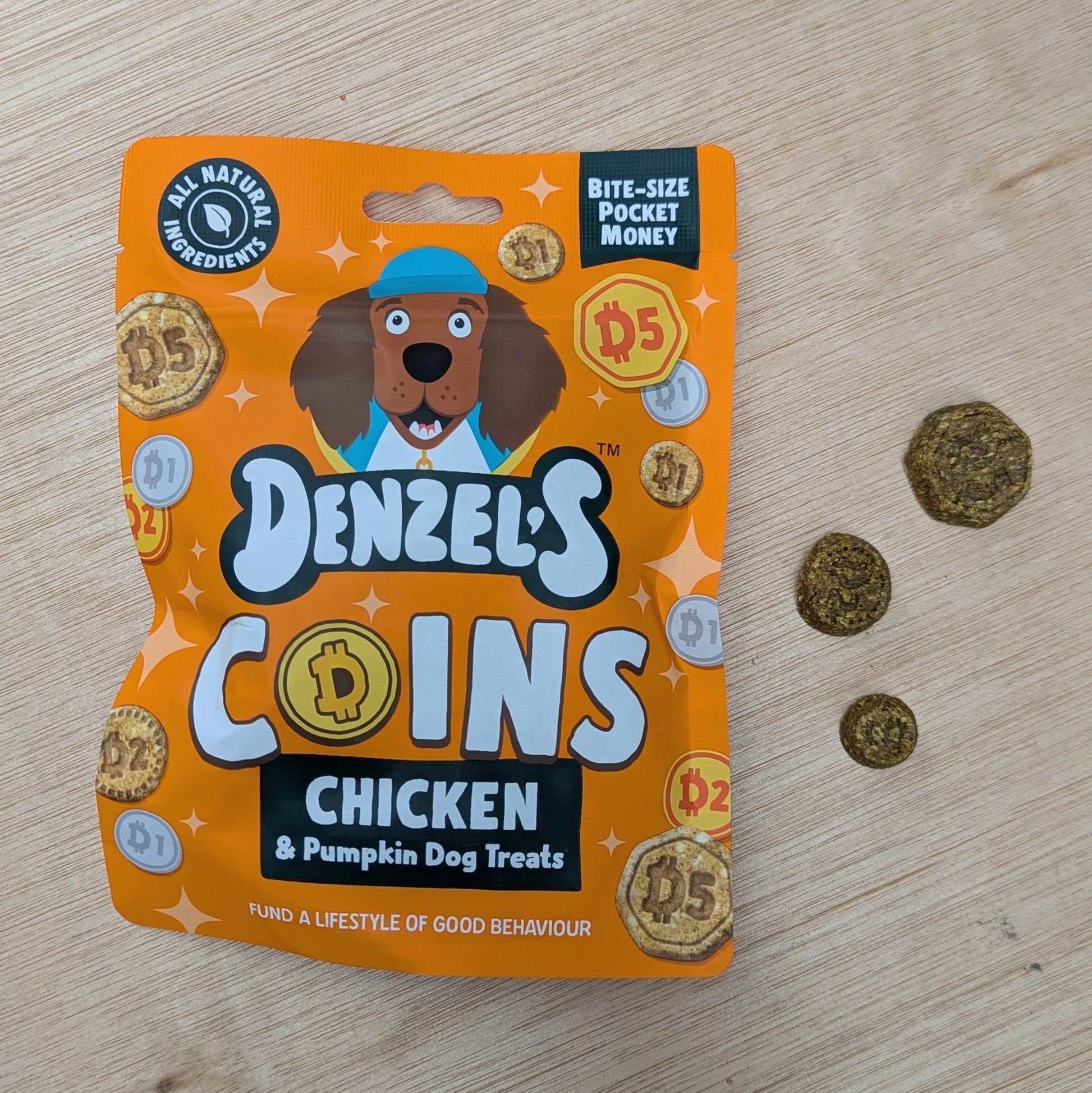 Denzel's Coins Chicken & Pumpkin Dog Treats packaging on a wooden surface with treats beside it on the right