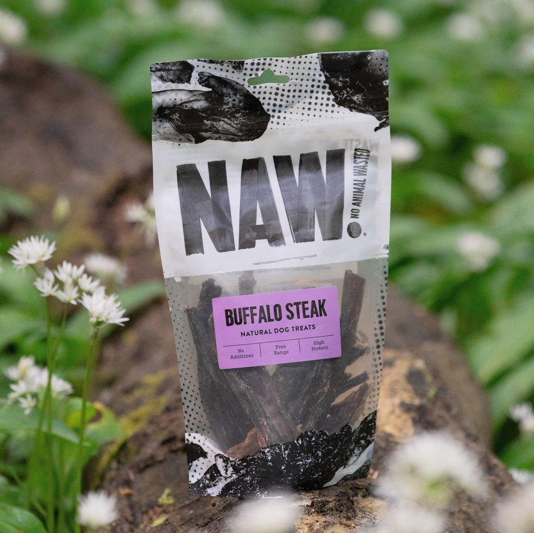 Package of NAW Buffalo Steak natural dog treats on a natural background with greenery and flowers.