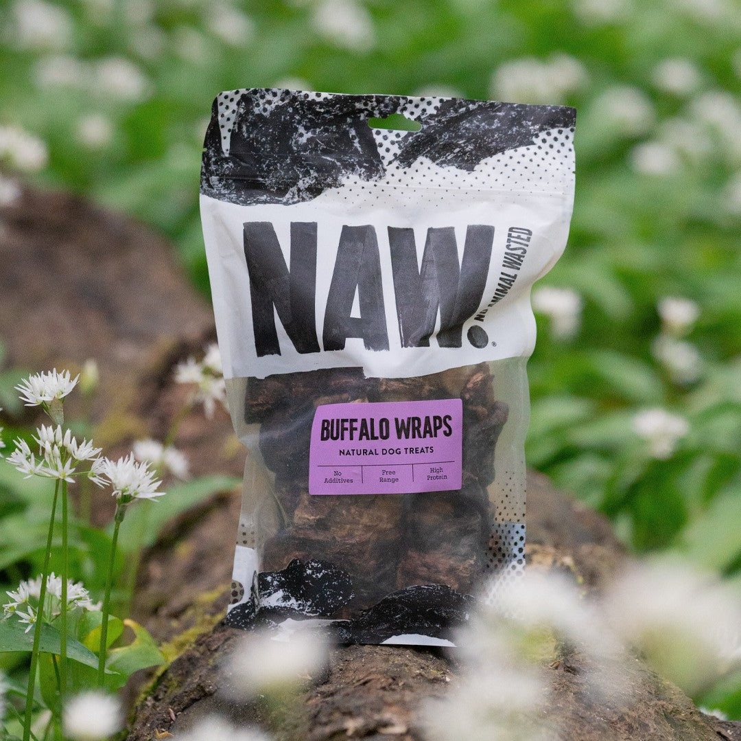 Bag of NAW Buffalo Wraps dog treats on a natural background with greenery and flowers.