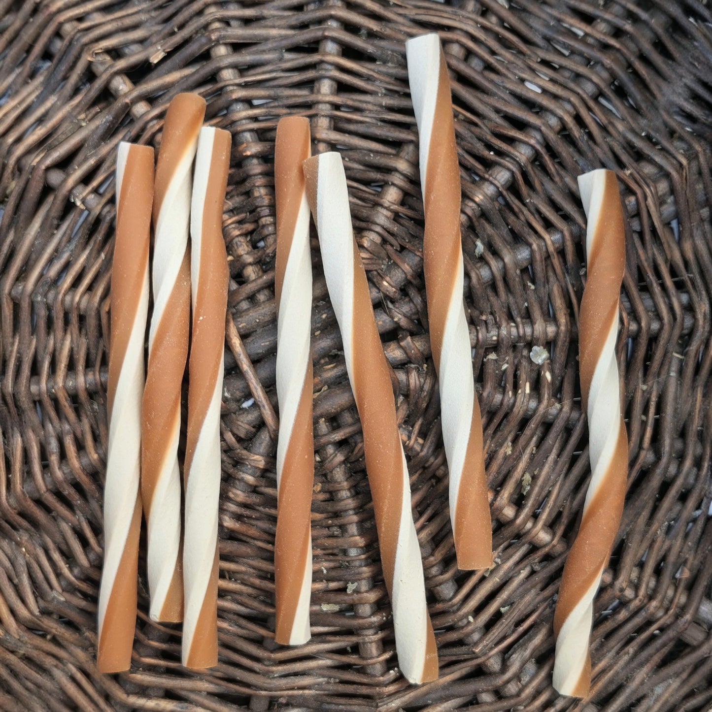 Twisted yellow and white chew sticks on a wicker surface