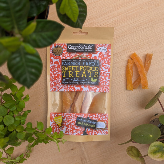 Package of Farmer Fred's Sweet Potato Treats for dogs on a wooden surface with plants around.