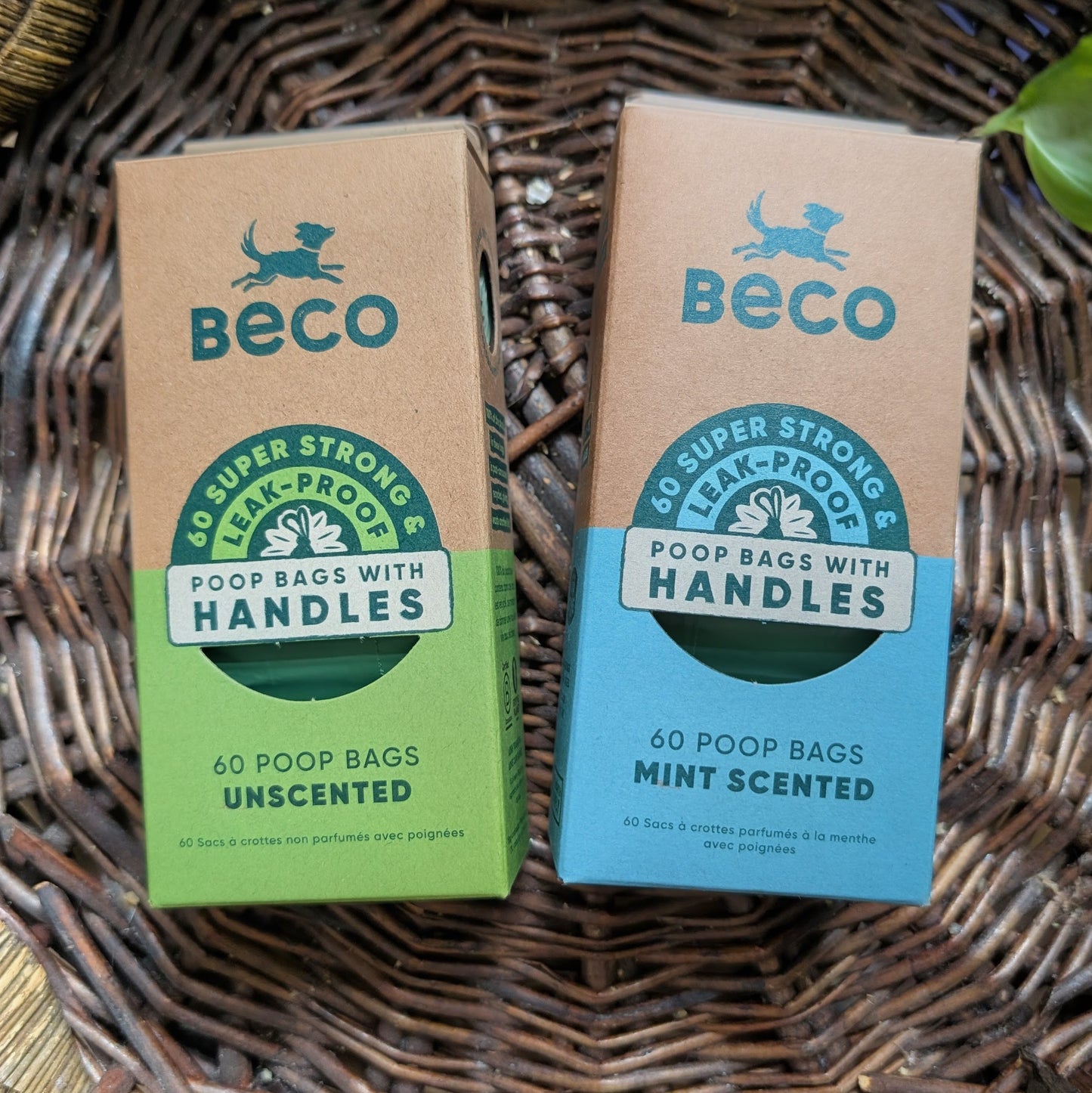 Two boxes of Beco poop bags with handles on a wicker surface. On the left is a a green unscented box and on the right is a blue mint scented box.