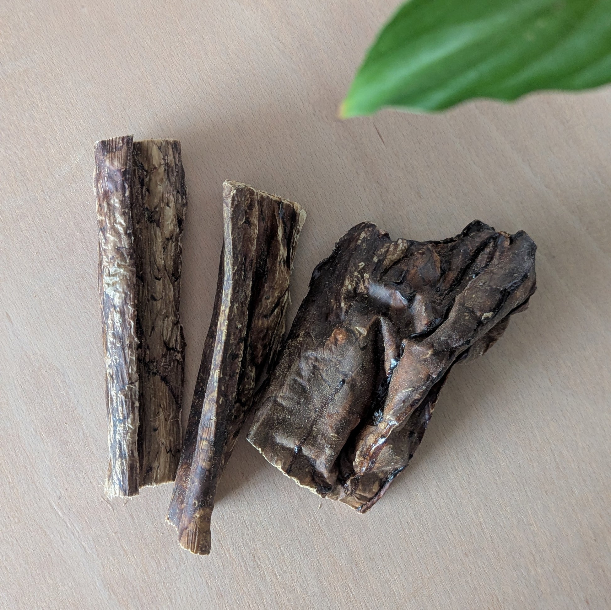 Three pieces of dried beef lung on a light surface with a green leaf in the corner. They are lying next to each other