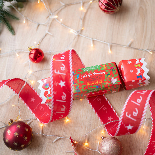 a festive print, red christmas cracker for dogs. It is made of cardboard, rectangular in shape. There is a white bauble at the bottom of the photo, a red one in the bottom right corner and a red and silver striped bauble at the top