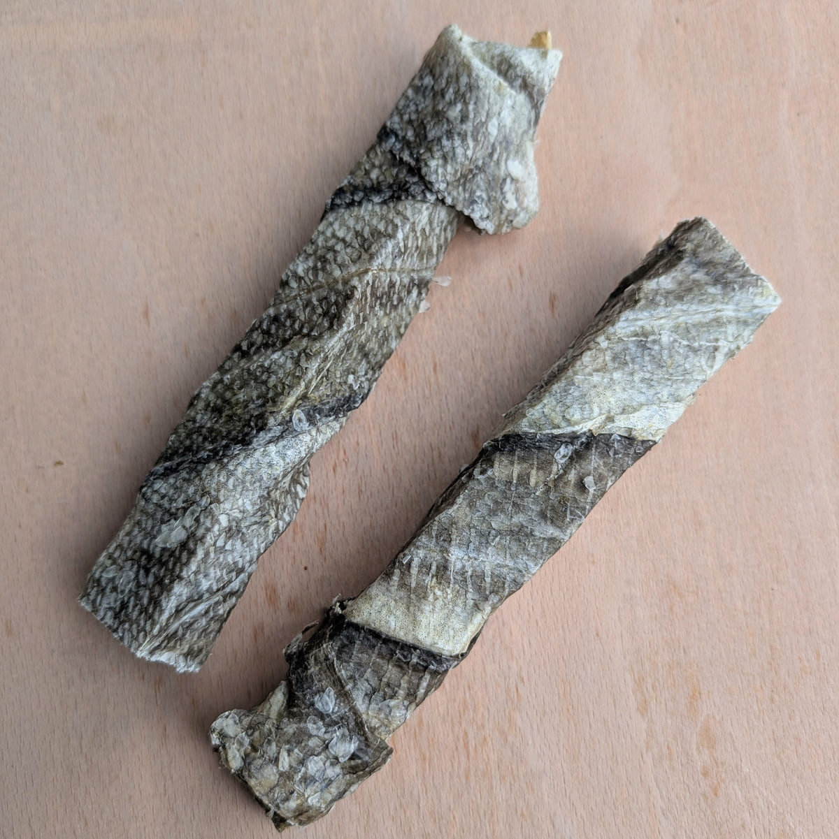 Two dried cod skin sticks laid diagonally on a light wood surface.