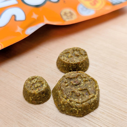 Three denzels coin treats on a wooden surface with the orange  treat bag in the background.
