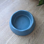 The ocean blue dog bowl is on a wooden table. The colour is between a light blue and a darker blue