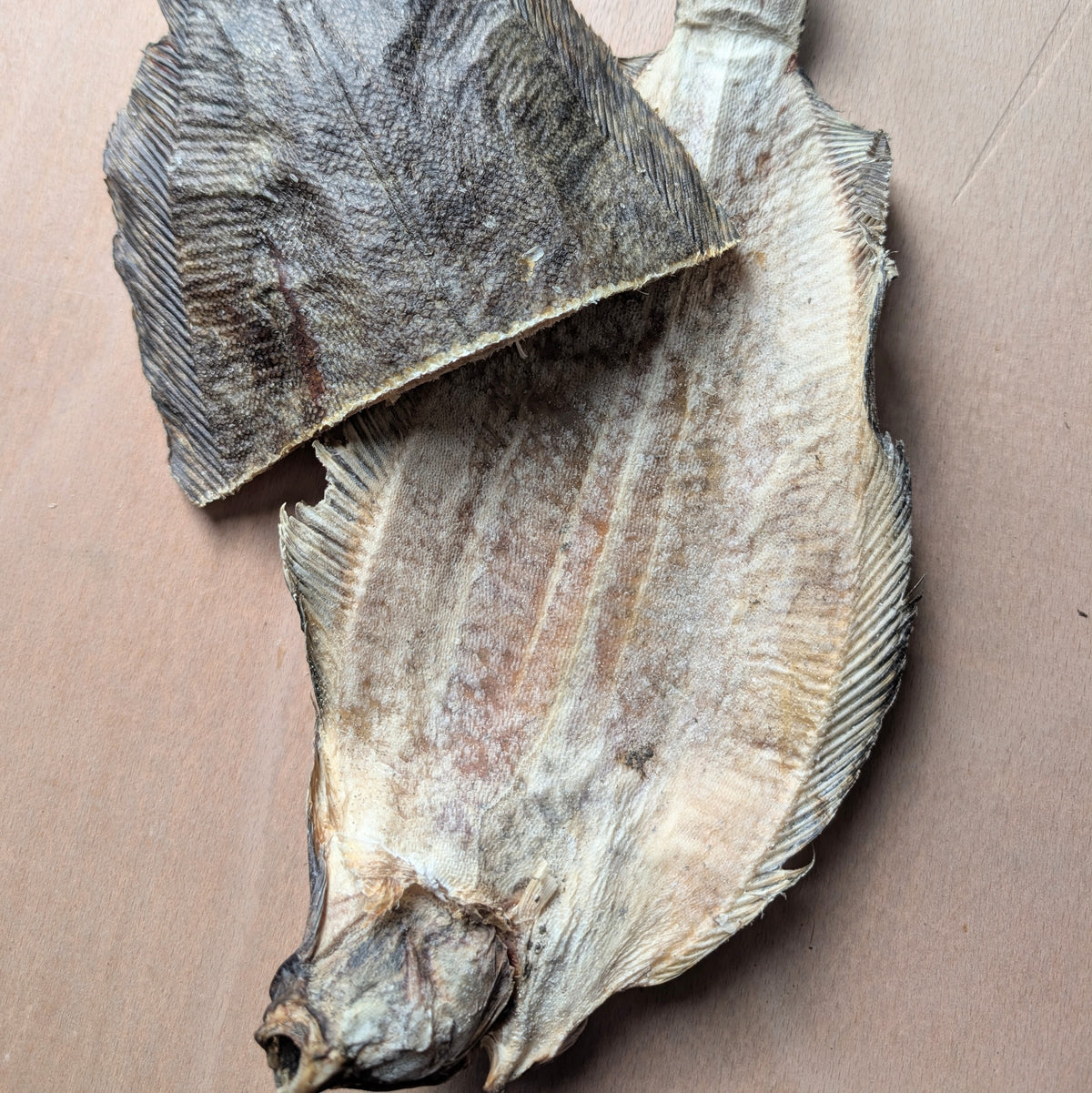 A dried whole sole fish on it's back, with a half sole fish on top, showing the otherside