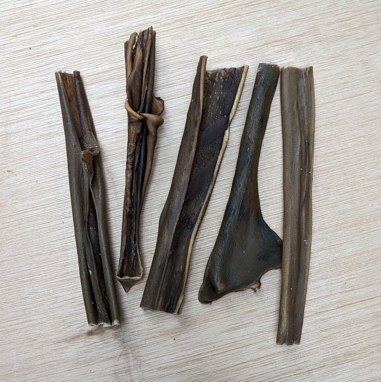 Five dried venison skins  lying next to each other on a light wooden surface